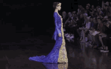 a woman in a blue and gold dress walks down the runway