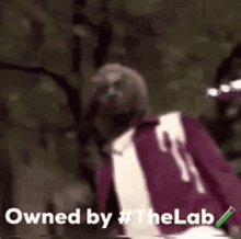 a man in a purple jacket and white shirt is standing in front of trees and says `` owned by the lab '' .