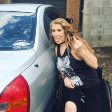 a woman in a wheelchair gives the middle finger in front of a silver car