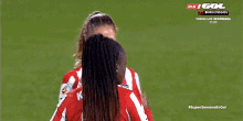 two female soccer players are hugging each other on a field and one of them has the number 2 on her jersey