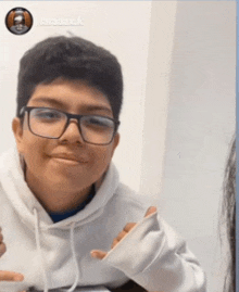 a young boy wearing glasses and a white hoodie smiles