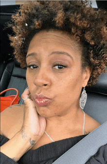 a woman with curly hair is wearing a seat belt and earrings