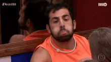 a man with a beard is wearing an orange tank top .