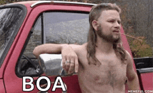 a shirtless man with a mullet is leaning against a red truck with the word boa written on it .