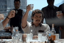 a man with a mustache is sitting at a table holding up a glass