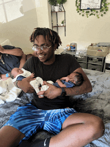 a man is holding two babies in his arms and smiling while sitting on a bed