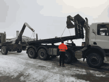 a man in an orange jacket is standing next to a dump truck with the number 11 on it