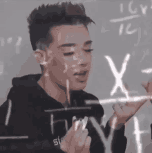 a man in a black hoodie is writing on a white board with x and y on it