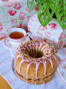 a bundt cake with pink frosting sits on a table with a cup of tea