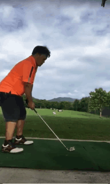 a man in an orange shirt is playing golf