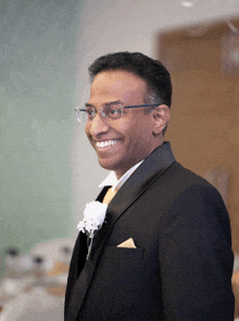 a man in a tuxedo with glasses and a yellow pocket square smiles