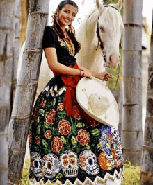 a woman in a dress with sugar skulls on it leans against a tree while riding a white horse