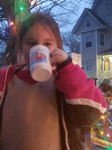 a little girl is drinking from a cup that says santa claus on it