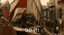 a group of people are standing on top of a pile of rubble holding a red flag and a sign that says do it .