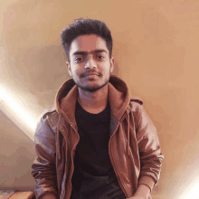 a young man wearing a brown jacket and a black shirt smiles for the camera