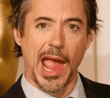 robert downey jr. is sticking his tongue out while wearing a suit and tie .