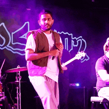 a man singing into a microphone while playing a guitar in front of a sign that says ' seam '