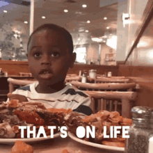 a young boy sitting at a table with plates of food and the words that 's on life written on the table