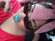 a woman wearing sunglasses and a red and white checkered headband is holding a blue lollipop in her mouth