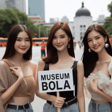 three women standing next to each other holding a sign that says museum bola