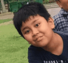 a young boy in a blue shirt is looking at the camera while standing in the grass .