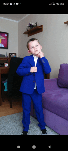 a young boy wearing a blue suit is standing in front of a purple couch