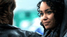 a woman with curly hair smiles at a man in a black jacket