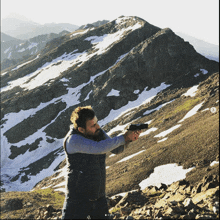 a man is holding a gun in front of a snowy mountain