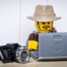 a lego man in a hat is sitting in front of a laptop .