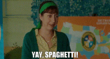 a woman in a green sweater and green headband is smiling and saying yay , spaghetti .