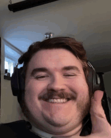 a man with a mustache wearing headphones is smiling and giving a thumbs up