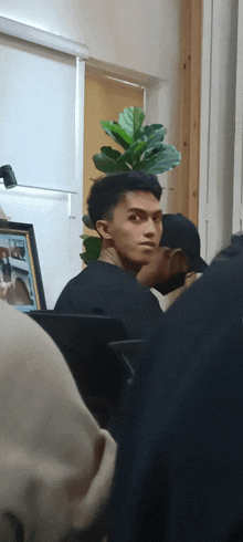 a man in a black shirt stands in a room with a plant in the background