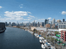 a row of boats are docked on the shore of a river with a city skyline in the background