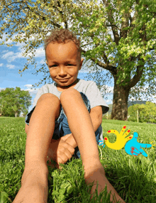 a young boy is sitting in the grass with a yellow hand with red nails on it