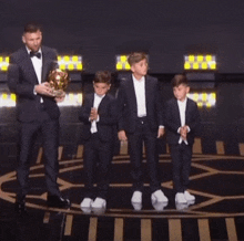 a man in a tuxedo is holding a trophy while three young boys stand behind him