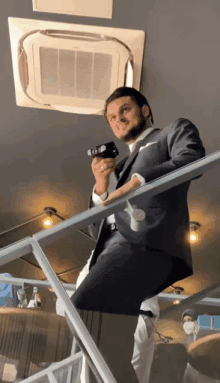 a man in a suit sits on a railing holding a camera