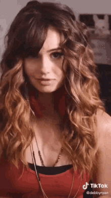 a woman with long curly hair is wearing headphones and a red tank top with a tiktok watermark