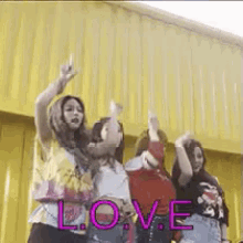 a group of young women are dancing together in front of a yellow curtain with the word love written on it .