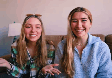 two women are sitting next to each other on a couch and smiling at the camera .