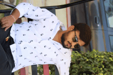 a man wearing sunglasses and a white shirt is sitting on a park bench