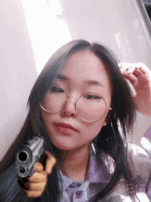 a girl wearing glasses is holding a gun in her hand