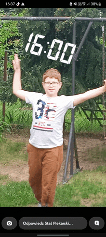 a boy is standing in front of a swing set with the time of 16:00