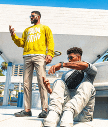 a man wearing a yellow sweatshirt with the word own on it is standing next to another man