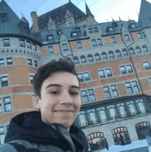 a young man taking a selfie in front of a large brick building