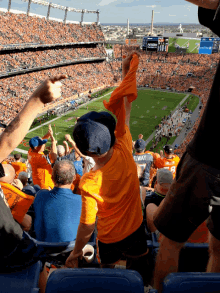 a boy in a yellow shirt with elway on the back of it stands in the stands at a football game