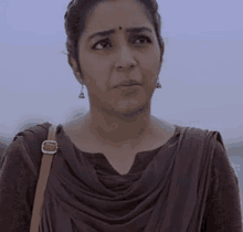 a woman wearing a brown dress and earrings is looking at the camera .