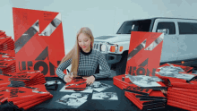 a woman sits at a table in front of a stack of red posters with the word leon on them