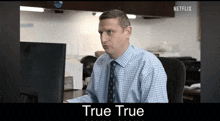 a man in a blue shirt and tie is sitting at a desk in front of a computer monitor .