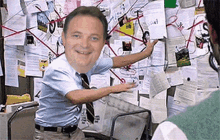 a man in a blue shirt and tie is standing in front of a bulletin board covered in papers .