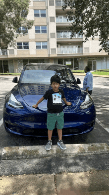 a young boy stands in front of a blue tesla